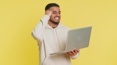 Heyecanlı mutlu Hintli adam dizüstü bilgisayarda yazıyor, proje üzerinde çalışıyor, sonuçların tadını çıkarıyor, piyango oyunu kazanıyor, başarıyı kutluyor, online alışveriş yapıyor, zafer kazanıyor. Sarı arka planda izole edilmiş Arap adam.