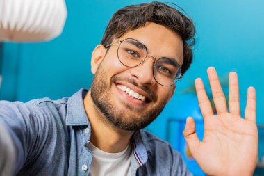 Hintli genç blog yazarının internet üzerinden akıllı telefondan selfie çekerken ve abonelerin sosyal medya için hikayeler kaydettiğini gösteren POV görüşü. Mutlu Arap adam cep telefonunu elleriyle tutuyor.