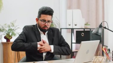 Stresli Hintli işadamı, modern ofis çalışma masasında çalışırken göğsünde kalp krizi geçirme riski bulunan gerilimden muzdarip. Resmi takım elbiseli erkek Hindu.