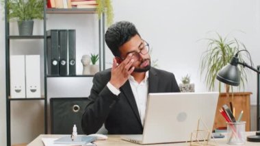 Hasta Hintli işadamı ofis masasında dizüstü bilgisayarla çalışırken göz yorgunluğu çektiği için acı çekiyor. Erkek Arap adam görme tedavisini geliştirmek için göz ilacı enjekte ediyor.