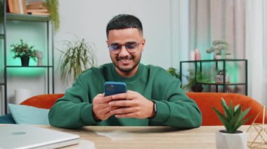 Masada oturan Hintli adam ofis odasındaki evinde cep telefonuyla gülümsüyor. Genç Arap adam akıllı telefon sosyal medya uygulamaları üzerinden rahatlama filmi izlerken mesajları paylaşıyor