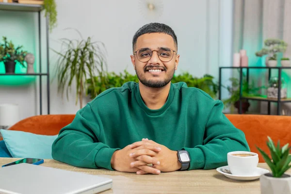Portrait of happy calm Indian man at home table smiling friendly, glad expression looking away dreaming resting, relaxation feel satisfied good news, celebrate win. Arabian young guy in office room
