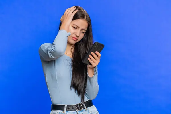 Woman use mobile phone smartphone typing browsing, loses becoming surprised sudden lottery results, bad fortune, loss, fail. Pretty brunette girl isolated alone on blue studio background, indoors