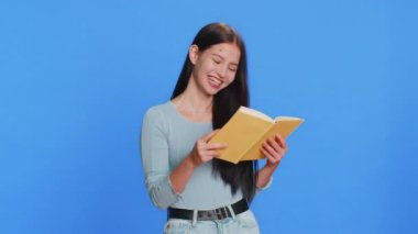 Mutlu, rahat gülümseyen, beyaz bir kadın komik bir masal kitabı okuyor, hobi, bilgi, bilgelik, eğitim, öğrenme, çalışma, vay be. Genç kız mavi arka planda izole edilmiş.