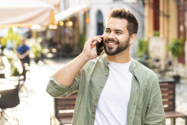 Erkek turistin uzaktan konuşma portresi akıllı telefondan arkadaşlarıyla iletişim kuruyor, şehir caddesinde beklenmedik bir şekilde iyi haber dedikodusu yapıyor. Şehir yaşam tarzları açık havada