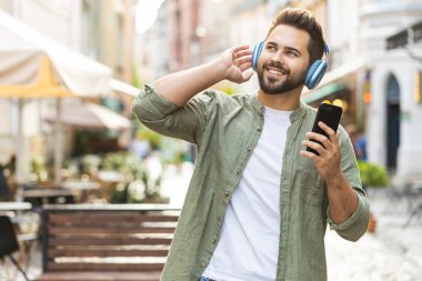 Kablosuz kulaklıklı, neşeli, neşeli beyaz adam dışarıda akıllı telefon dansında favori enerjik disko müziğini dinliyor. Turist, Sunshine City Caddesi 'nin önünden geçiyor.