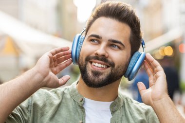 Kablosuz kulaklıklar takmış, açık havada dans eden enerjik disko rock n roll müziği dinleyen mutlu, gevşemiş Kafkas genci. Şehir Güneşi Sokağı arka planında duran adam.