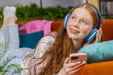 Kablosuz kulaklıklı, evinde kanepeye uzanmış, en sevilen disko müziği dinlemeyi seçen mutlu genç kız. İnsanlar hafta sonu boş zaman aktiviteleri