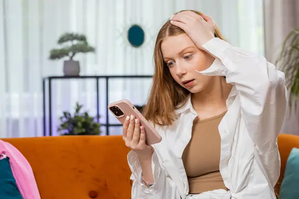 Teenager red hair girl use smartphone typing browsing, loses becoming surprised sudden lottery fail, exam results, bad news, fortune loss, fail, play online game. Child sits at home living room couch