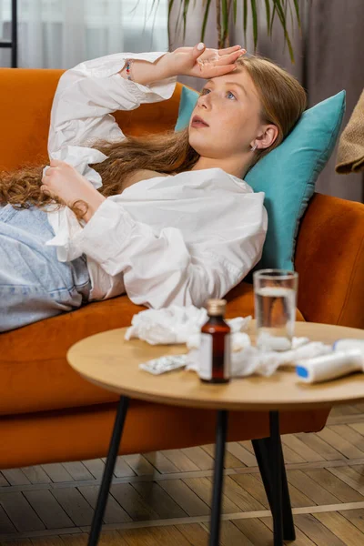 ティーンエイジャー病の赤い髪の少女は 自宅のリビングルームのソファーに横たわって風邪やアレルギーに苦しんでいます 病気の子供はナプキンにスニッツワイプを吹きます コロナウイルス検疫 パンデミック インフルエンザ バーティカル ロイヤリティフリーのストック写真