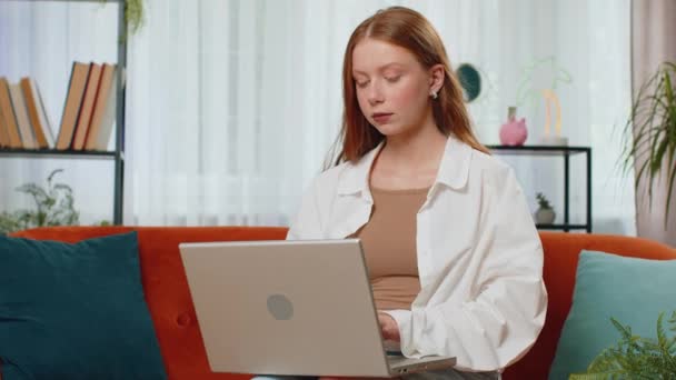 ティーンエイジャー赤毛少女は 自宅で仕事の勉強教育を終えた後 ノートパソコンを閉じるソファに座っています オンラインで働く子供のフリーランサー 遠隔仕事 Eラーニング ノートパソコンでの閲覧 — ストック動画