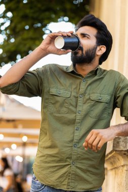 Mutlu sakallı Hintli genç adam sabah kahvesinin tadını çıkarıyor. Sıcak bir içecek, şehir hayatı tarzında. Dinleniyorum, ara veriyorum. Gülümseyen Arap Müslüman yetişkin adam şehir merkezi caddesinde duruyor. Dikey