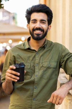 Mutlu sakallı Hintli genç adam sabah kahvesinin tadını çıkarıyor. Sıcak bir içecek, şehir hayatı tarzında. Dinleniyorum, ara veriyorum. Gülümseyen Arap Müslüman yetişkin adam şehir merkezi caddesinde duruyor. Dikey