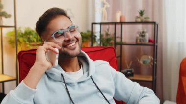 Telefon, iyi haber, dedikodu. Mutlu Hintli adam akıllı telefondan hoş sohbetler ediyor, modern ev odasındaki arkadaşlarıyla konuşmaktan keyif alıyor. Cep telefonundan hoşlanan adam konuşuyor