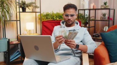 Planlama bütçesi. Zengin, mutlu Hintli adam para sayıyor dizüstü bilgisayar kullanıyor evde faturaları hesaplıyor. Arap adam kazancından memnun, planlı tatil için para biriktiriyor, hediyeler