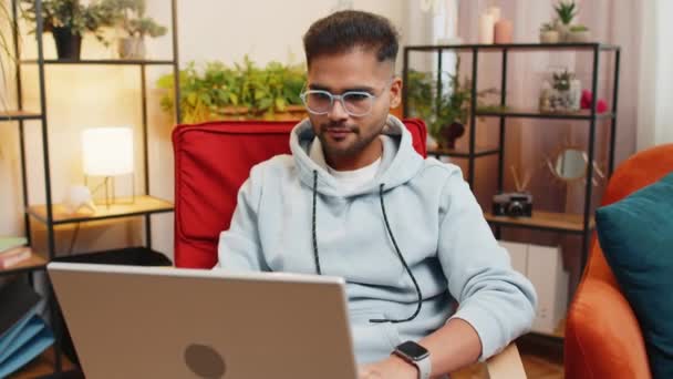 印度男子在客厅完成工作后 坐在椅子上关闭笔记本电脑 年轻的阿拉伯自由职业者在家里的椅子上做远程在线工作 电子学习 在笔记本电脑上浏览互联网 — 图库视频影像
