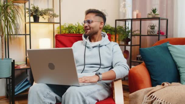 印度男人在看笔记本电脑 和朋友或家人一起做视频摄像头电话会议 在现代化的家庭公寓里享受愉快的对话 阿拉伯人笑了 挥挥手打招呼坐在椅子上 — 图库视频影像