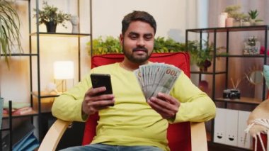 Planlama bütçesi. Zengin, mutlu Hintli bir adam akıllı telefon hesap makinesi kullanıyor. Para sayıyor, ev faturalarını hesaplıyor. Kazancından memnun olan adam, planlı hediyeler için para biriktirir.