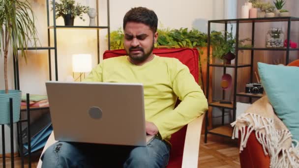 不满的印度男人用笔记本电脑打字上网工作 输了意外的彩票结果坏消息运气损失游戏失败的电脑病毒 坐在家里房间椅子上的阿拉伯人 — 图库视频影像