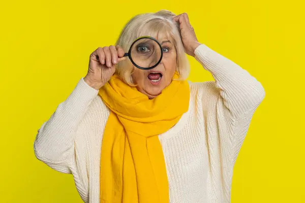 研究者 科学者 シニア 顔の近くに壮大なガラスを保持し 大きなズームされた面白い目でカメラを調べ 分析します 黄色の背景にある高齢のおばあちゃん ストック写真