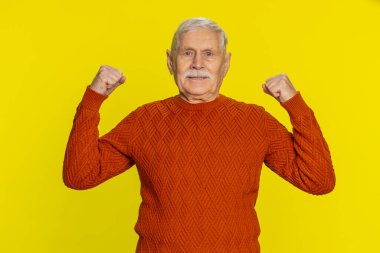 Ben güçlü ve bağımsızım. Yaşlı kıdemli adam kaslarını gösteriyor ve kendinden emin görünüyor. Haklar için savaşmak için güç hissediyor. Başarılı olmak için enerji kazanıyor. Büyükbabam sarı arka planda izole edilmiş.