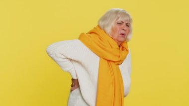 Yaşlı bir kadın sırt ağrısı çekiyor, masaj yapıyor alt omurgasına masaj yapıyor, dayanılmaz spazm yüzünden kaşlarını çatıyor kasları ve tendonları yırtılıyor, böbrek taşları, sinir sıkışması. Sarı arka planda büyükanne emeklisi.