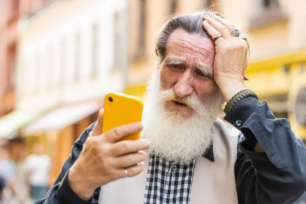Senior old man use smartphone typing browsing, loses becoming surprised sudden lottery results, bad news, fortune loss, fail. Elderly grandfather walking in urban city street outdoors. Town lifestyles