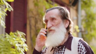 Yetişkin turist kıdemli adam arkadaşlarıyla uzaktan iletişim kuruyor. Yaşlı büyükbaba telefonda konuşuyor. Habersiz dedikodu. Şehir caddesinde yürüyor.