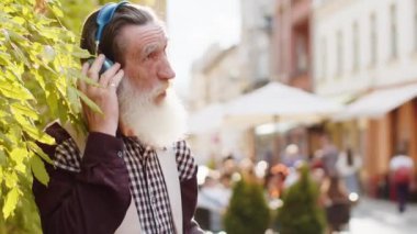 Neşeli, gevşemiş, sakallı, kablosuz kulaklıklı yaşlı adam dışarıda dans eden enerjik disko rock 'n roll müziğini dinliyor. Yaşlı büyükbaba şehir caddesinde yürüyor