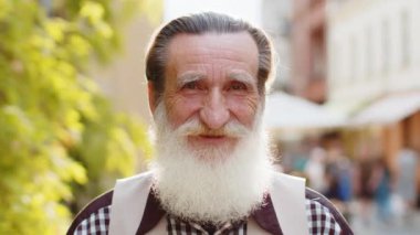 Mutlu sakallı yaşlı bir adamın portresi dostça gülümsüyor, kameraya bakan mutlu yüz ifadesi hayal kuruyor, dinleniyor, rahatlıyor dışarıda iyi haberler veriyor. Şehir caddesinde yaşlı büyükbaba