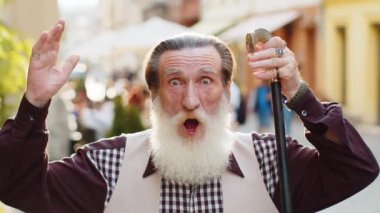 Aman Tanrım, vay canına. Sakallı yaşlı adam kameraya şaşkın şaşkın bakıyor. Aniden kazanılan piyango galibiyeti karşısında şaşırdı. Açık havada iyi haberler var. Yaşlı büyükbaba şehir caddesinde