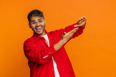 Hintli adam savurma israfını gösteriyor paylaşma parası, daha fazla bahşiş, büyük kar, piyango ikramiyesi kazanma, başarılı alışveriş ödeme nakiti. Turuncu arka planda izole edilmiş Arap Hindu adam.