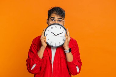 Ofis saatinin arkasına saklanan katı bir Hintli adam vardiyasını kontrol ediyor, işe geç kalıyor son teslim tarihi belirsiz bir yüz. Turuncu arka planda izole edilmiş Arap bir adam. Kopyalama alanı