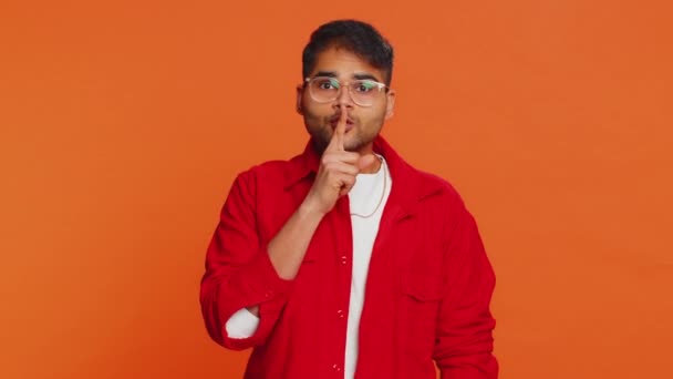 静かにしてください インドの男は唇にインデックスフィンガーを押し 沈黙のジェスチャーのサインは秘密を告げず 話すゴシップをやめ 機密のプライバシーを停止します オレンジ色の背景に孤立したアラビアの若い男 — ストック動画