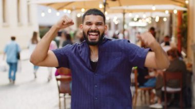 Sakallı genç adam bağırıyor, başarıyı kutluyor, kazanıyor, gol başarısı, iyi haber, piyango talihi, açık havada zafer. Şehirdeki Sunshine Sokağı 'nda yürüyen Hintli adam. Kasaba yaşam tarzları