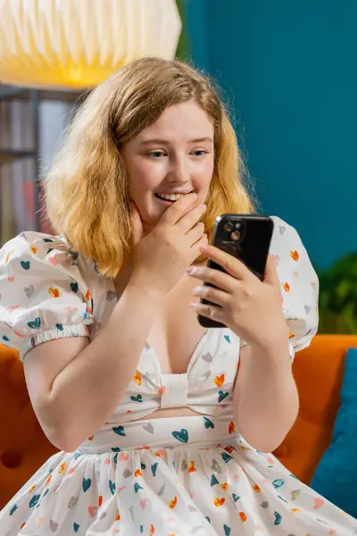 Happy young woman use mobile smartphone typing browsing say wow yes found out great big win good news celebrate lottery jackpot, play victory game. Adult girl at home in room sits on sofa. Vertical