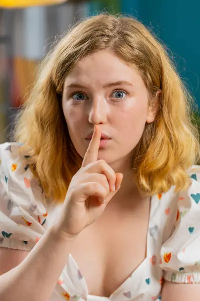 Keep my secrets, silence. Redhead woman whisper news rumors holding hands near mouth, share gossip, quiet. Red hair adult girl telling interesting confidential story at home room on couch. Vertical
