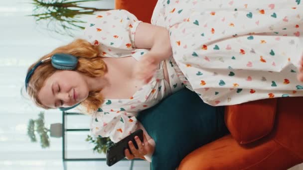 Rudowłosa Szczęśliwa Kobieta Bezprzewodowych Słuchawkach Relaksująca Się Kanapie Domu Wybierając — Wideo stockowe