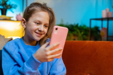 Akıllı telefon sosyal medya uygulamaları üzerinden mesajlaşan genç kız rahatlama filmi izliyor. Mutlu ergen çocuk evde cep telefonu kullanıyor. Akşam vakti kanepede oturuyor.