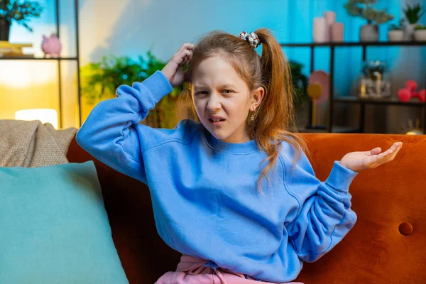 What. Why. Caucasian child girl raising hands in indignant expression, asking reason of failure demonstrating disbelief irritation by troubles. Female teenager kid at night home in living room on sofa