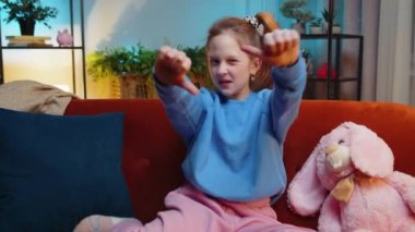 Hoşlanmamak. Mutsuz çocuk kız işaret dilini gösteriyor, hoşnutsuzluğunu dile getiriyor, hoşnutsuzluğunu dile getiriyor, modern apartman dairesinde tatminsiz kötü işler yapıyor. Akşam odasındaki kanepede hoşnutsuz genç çocuk.