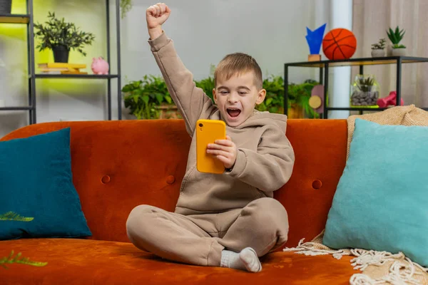 Happy child boy use mobile smartphone typing playing browsing found out great big surprise good positive news celebrate online game win. Excited teenager little kid at home in living room sits on sofa