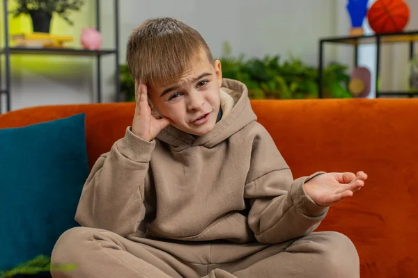 What. Why. Young child kid boy raising hands in indignant expression, asking reason of failure demonstrating disbelief irritation by troubles. Male Caucasian teenager at home in living room on sofa