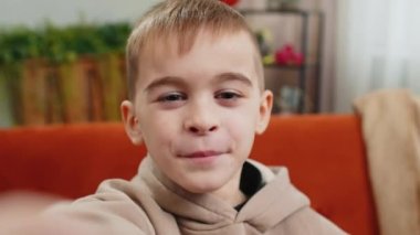 Kafkas çocuk blogcu POV 'u akıllı telefondan selfie çekiyor, sosyal medya aboneleriyle online video görüşmesi yapıyor. Genç bir erkek çocuk evde video kaydı yapıyor. Kanepede oturuyor.