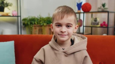 Mutlu gülümseyen Kafkas ergen liseli çocuğun yakın plan portresi. 8 yaşında. Küçük sevimli sarışın çocuk, evde kameraya bakıyor. Oturma odasında turuncu koltukta oturuyor.