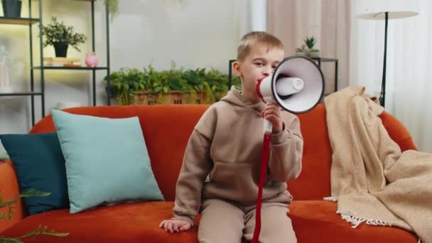未成年男孩用扩音器说话 宣布新闻 用扩音器大声宣布广告警告 家里客厅公寓沙发上的少年男孩儿 — 图库视频影像