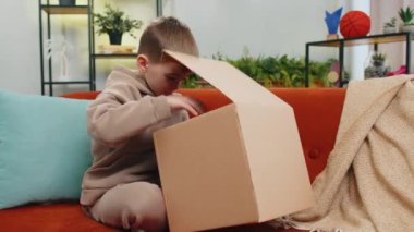 Öfkeli, hoşnutsuz, paketlerini açan çocuk üzgün ve kafası karışmış bir şekilde çevrimiçi bir mağazadan gelen yanlış teslimat, kötü kalitede bozuk alışveriş. Çocuk odada, kanepede.