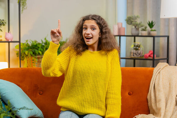 Eureka. Thoughtful clever inspired child girl make gesture raises finger came up with creative plan feels excited with good idea inspiration motivation, question at home apartment. Kid sits on sofa