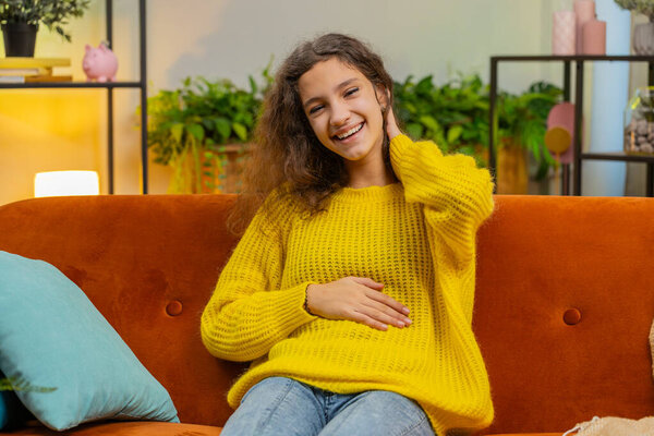 Child girl laughing out loud after hearing ridiculous anecdote, funny joke, feeling carefree amused positive people lifestyle at home apartment. Teenager female 14-15 years kid in living room on couch