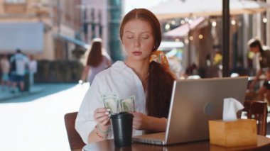 Serbest çalışan mutlu bir kız para sayıyor, hesap makinesi uygulaması kullanıyor, dışarıda otelden yemek sipariş etmeyi planlıyor. Şehir kafeteryasındaki masada oturan genç bayan turist